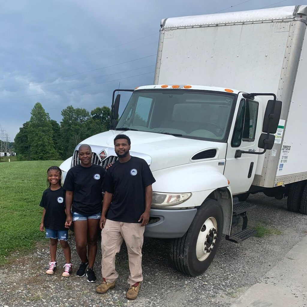 Billy and Shikira standing in front of a truck with their daughter